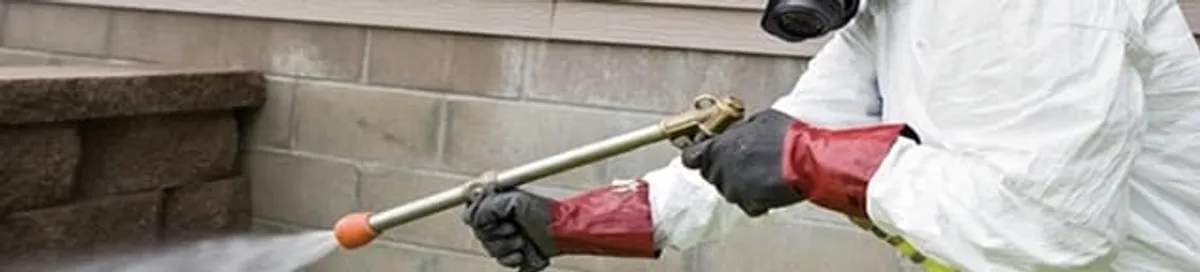 Pest control technician applying exterior insect treatment along a home foundation in Wichita, KS
