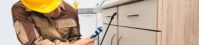 Roach exterminator applying treatment under kitchen cabinets in Wichita, KS