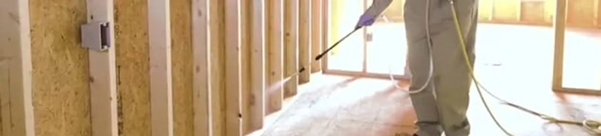 Termite treatment technician applying spray along framing and unfinished walls in Wichita, KS