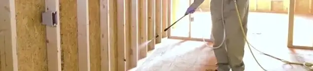 Termite treatment technician applying spray along framing and unfinished walls in Wichita, KS